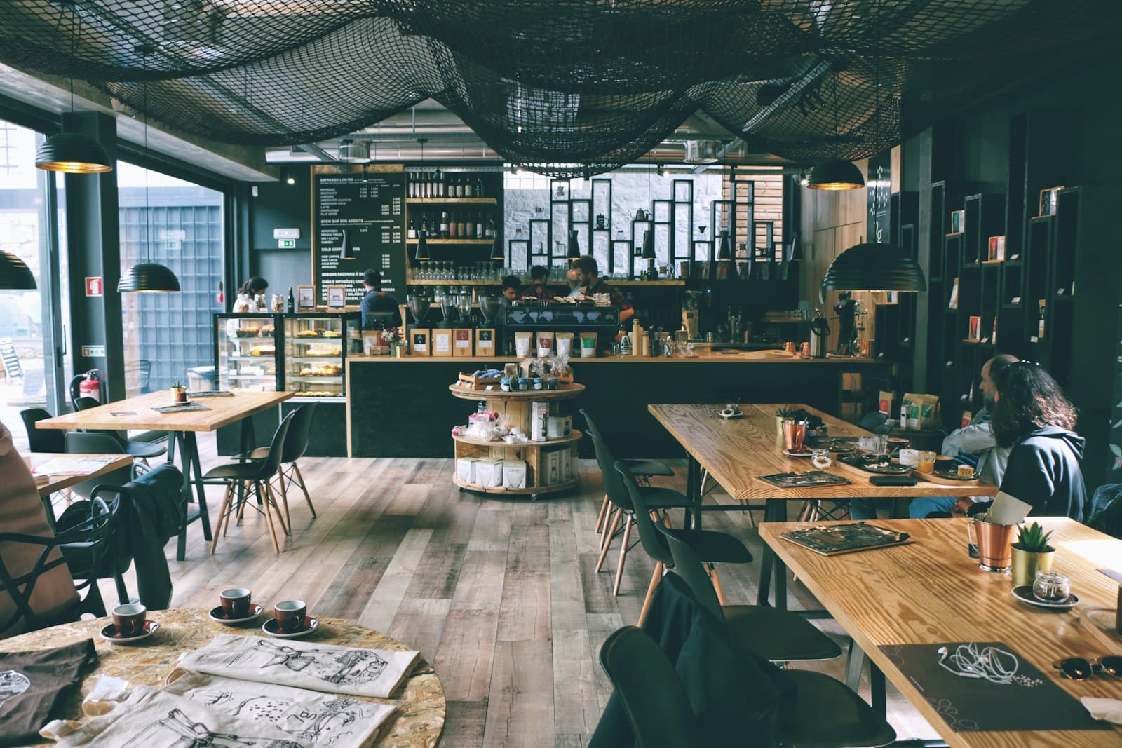 Salle du café au mobilier de bois clair sous une verrière industrielle